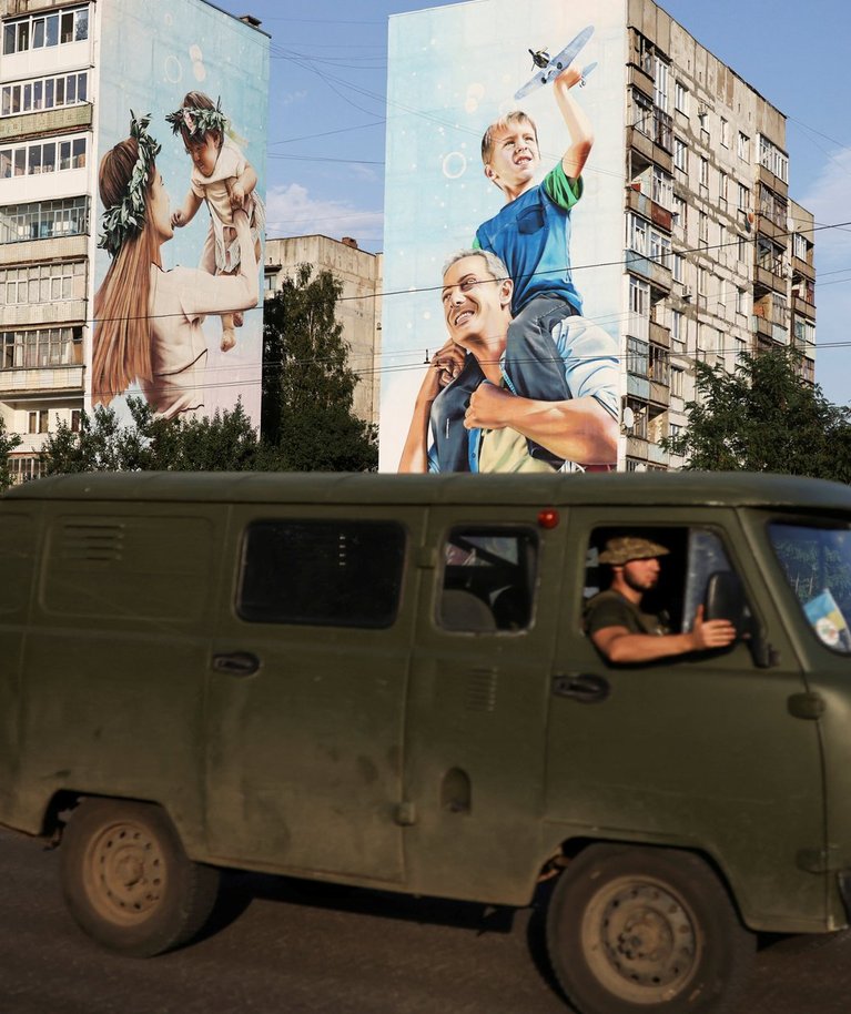 Ukraina sõjaväelased sõidavad Bahmuti linnas mööda kahjustatud hoonetest, kus on maja peal joonistusega kujutatud perekonda. Foto tehtud 14. augustil 2022. 