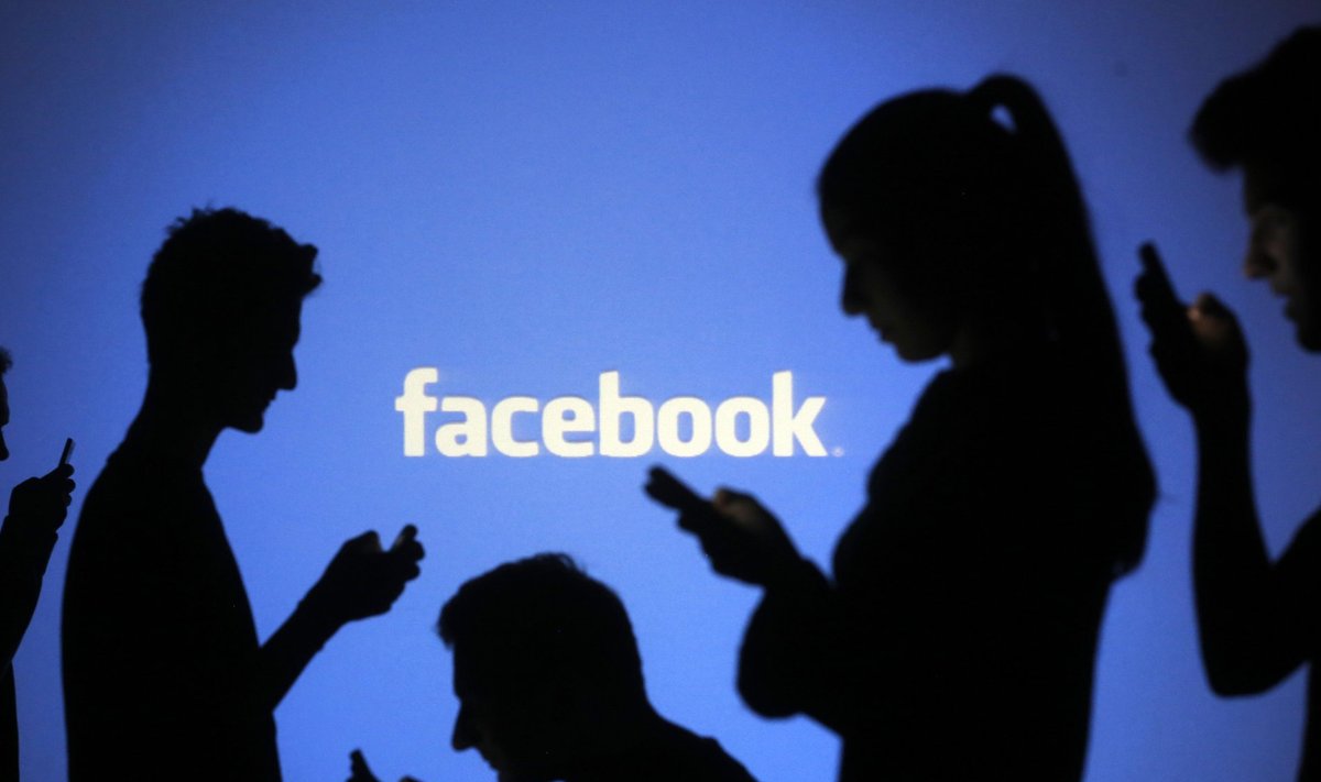 People pose with mobile devices in front of projection of Facebook logo in this picture illustration taken in Zenica