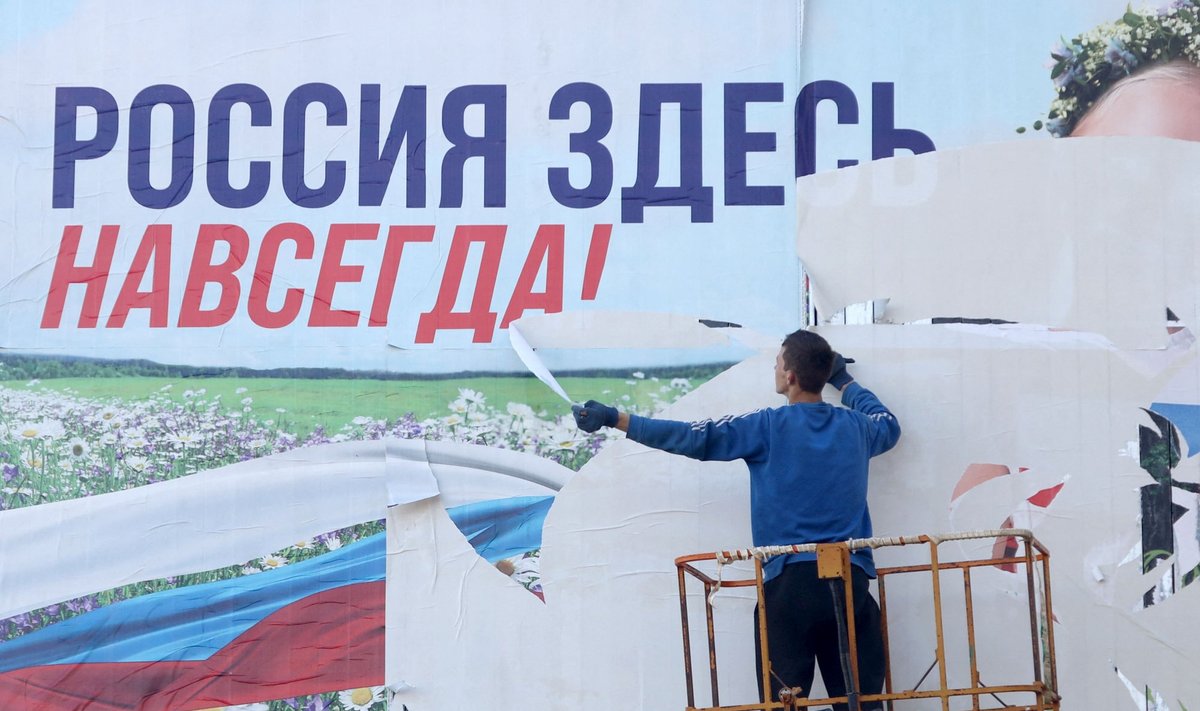 Tagasivallutatud Hersoni linnas rebib tööline ära plakatit, millel on kirjas "Venemaa on igavesti siin". Foto on tehtud 14. novembril 2022.