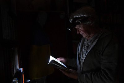 Physicist Igor Žuk (70) reads a book using a headlamp at his home in North Kyiv.