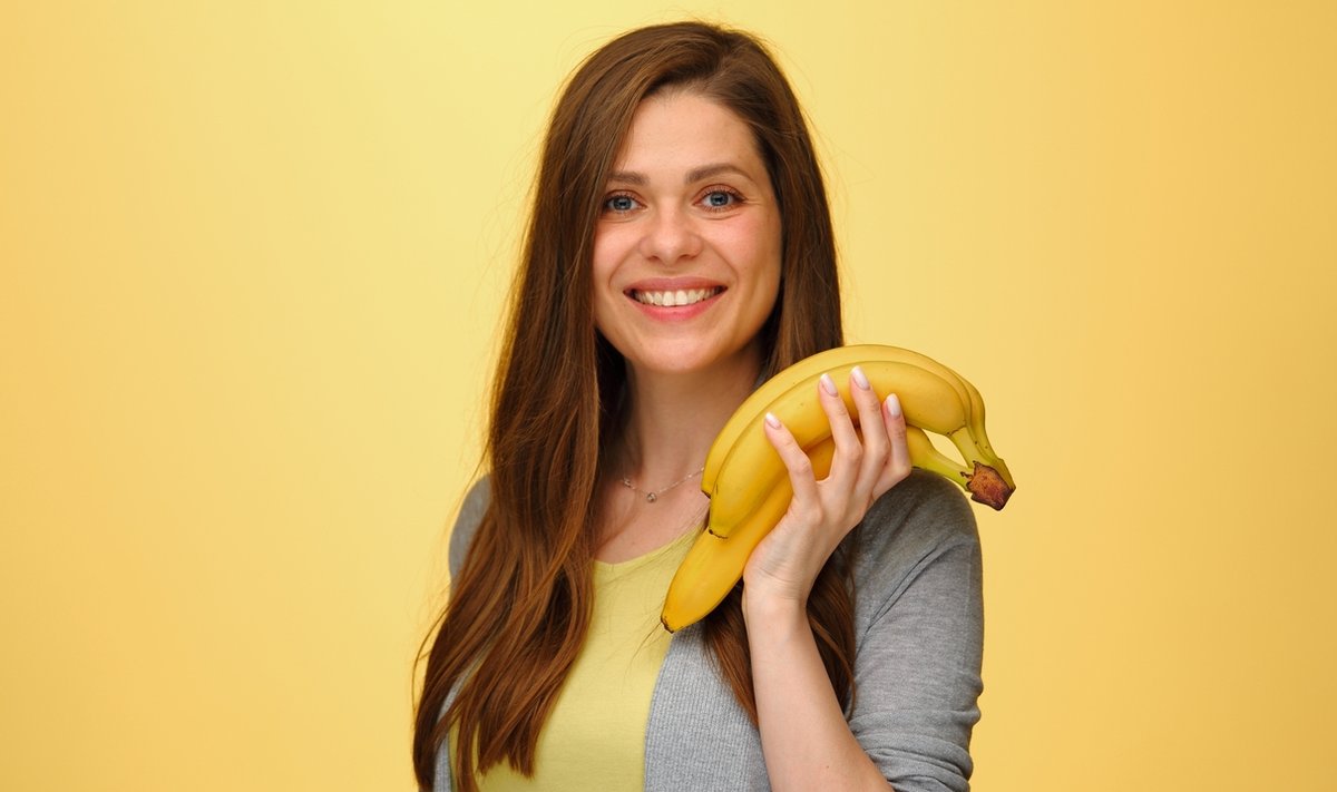 Smiling,Woman,Holding,Bananas,Fruits,Isolated,On,Yellow,Studio,Back.