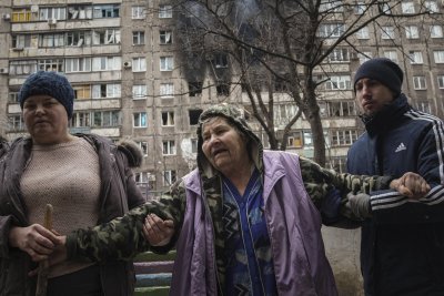 Inimesed aitavad naisel kõndida, taustal pommitatud kortermaja